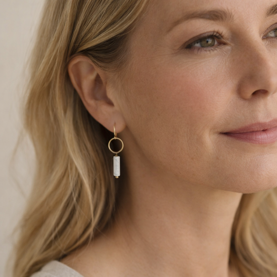 Close-up of a woman wearing gold hoop earrings with a white stone.