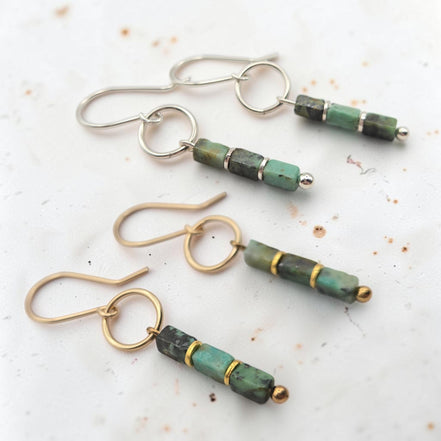 Three pairs of handmade dangle earrings on a light, textured white background. The earrings feature natural green and dark gray stone beads with polished gold and silver-tone metal findings.