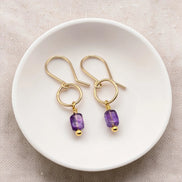 Gold earrings with purple amethyst beads on a white dish