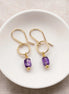 Gold earrings with purple amethyst beads on a white dish