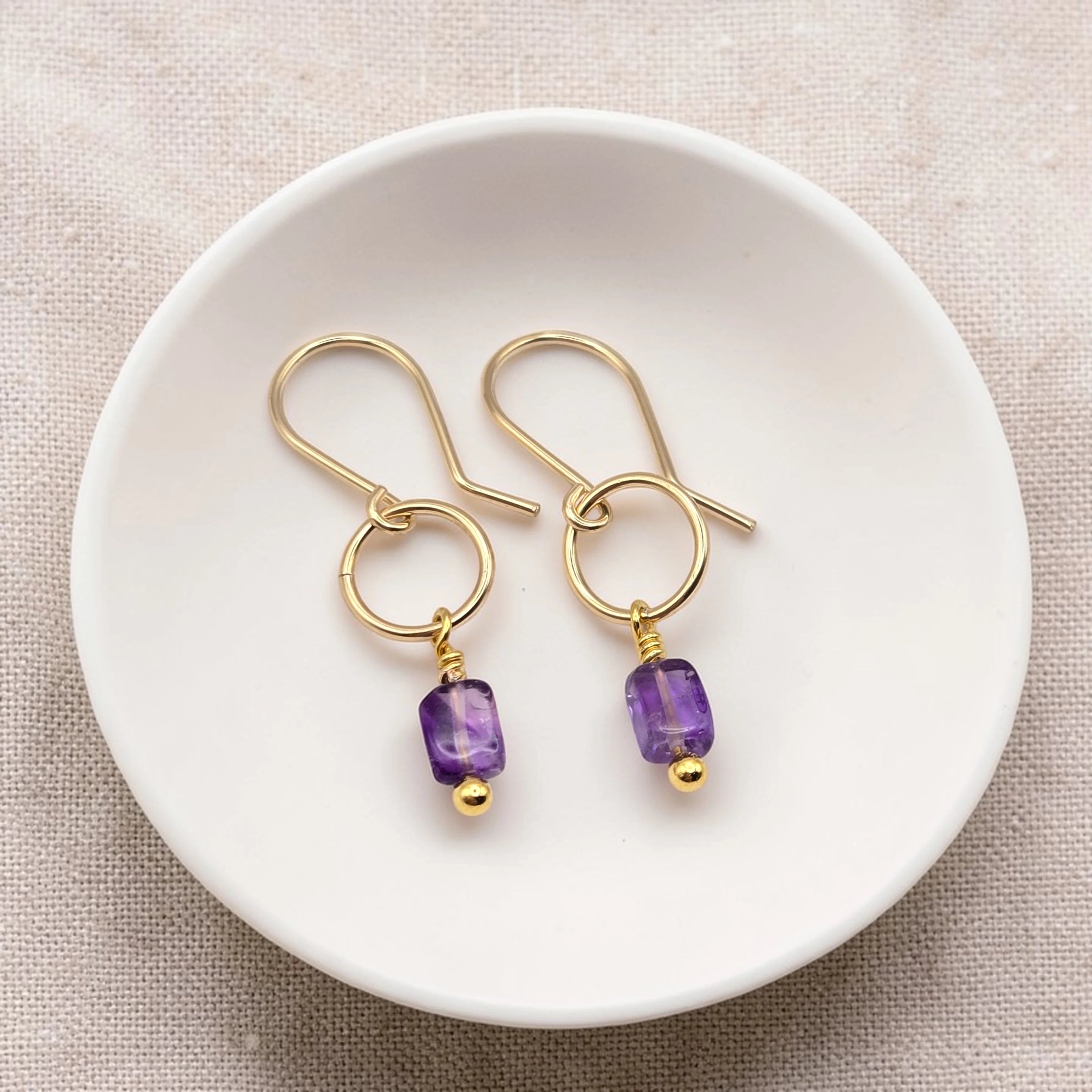 Gold earrings with purple amethyst beads on a white dish