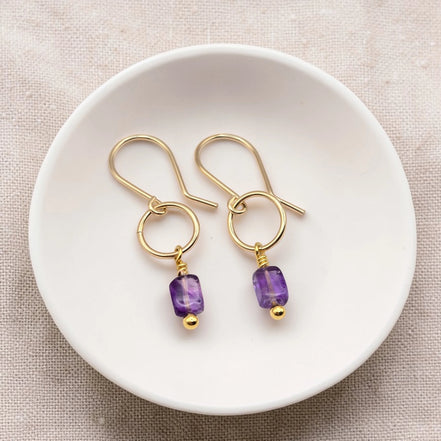 Gold earrings with purple amethyst beads on a white dish