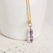 Gold necklace with purple beads on a white background