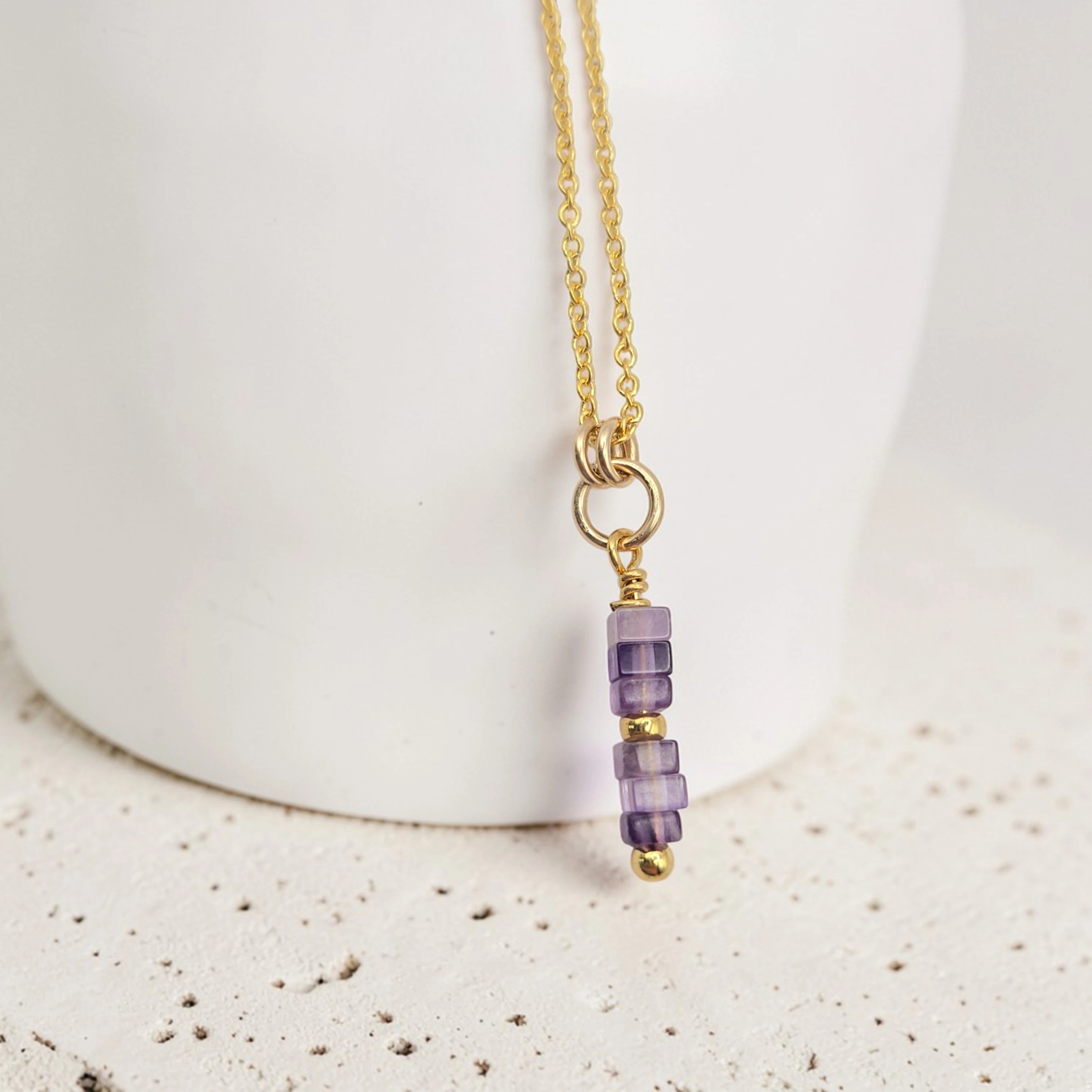 Gold necklace with purple beads on a white background