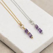 Two necklaces with amethyst beaded pendants on a white stone surface.