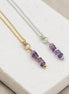 Two necklaces with amethyst beaded pendants on a white stone surface.