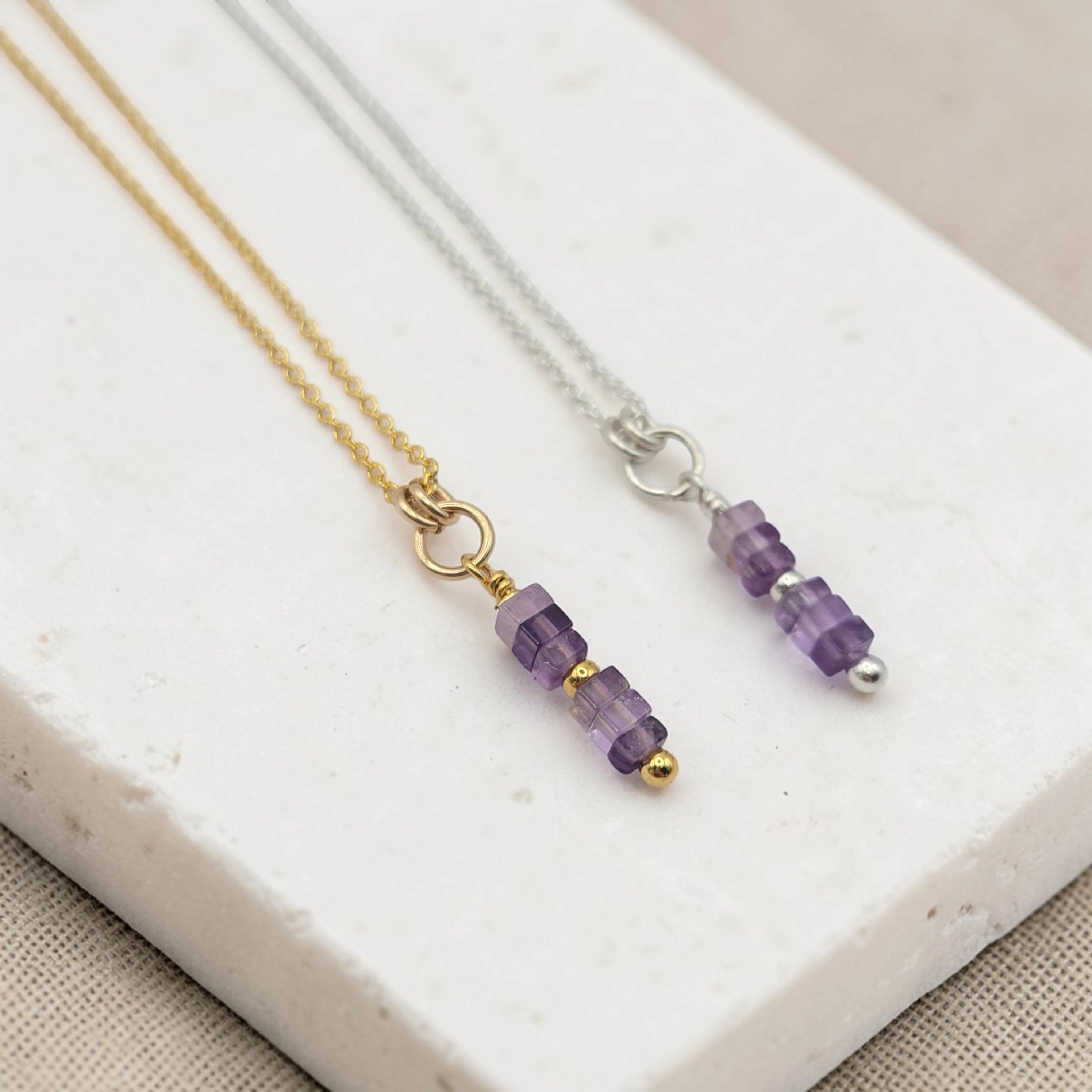 Two necklaces with amethyst beaded pendants on a white stone surface.