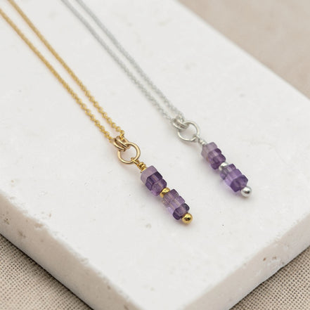 Two necklaces with amethyst beaded pendants on a white stone surface.