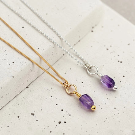 Two necklaces with purple beads on a textured surface