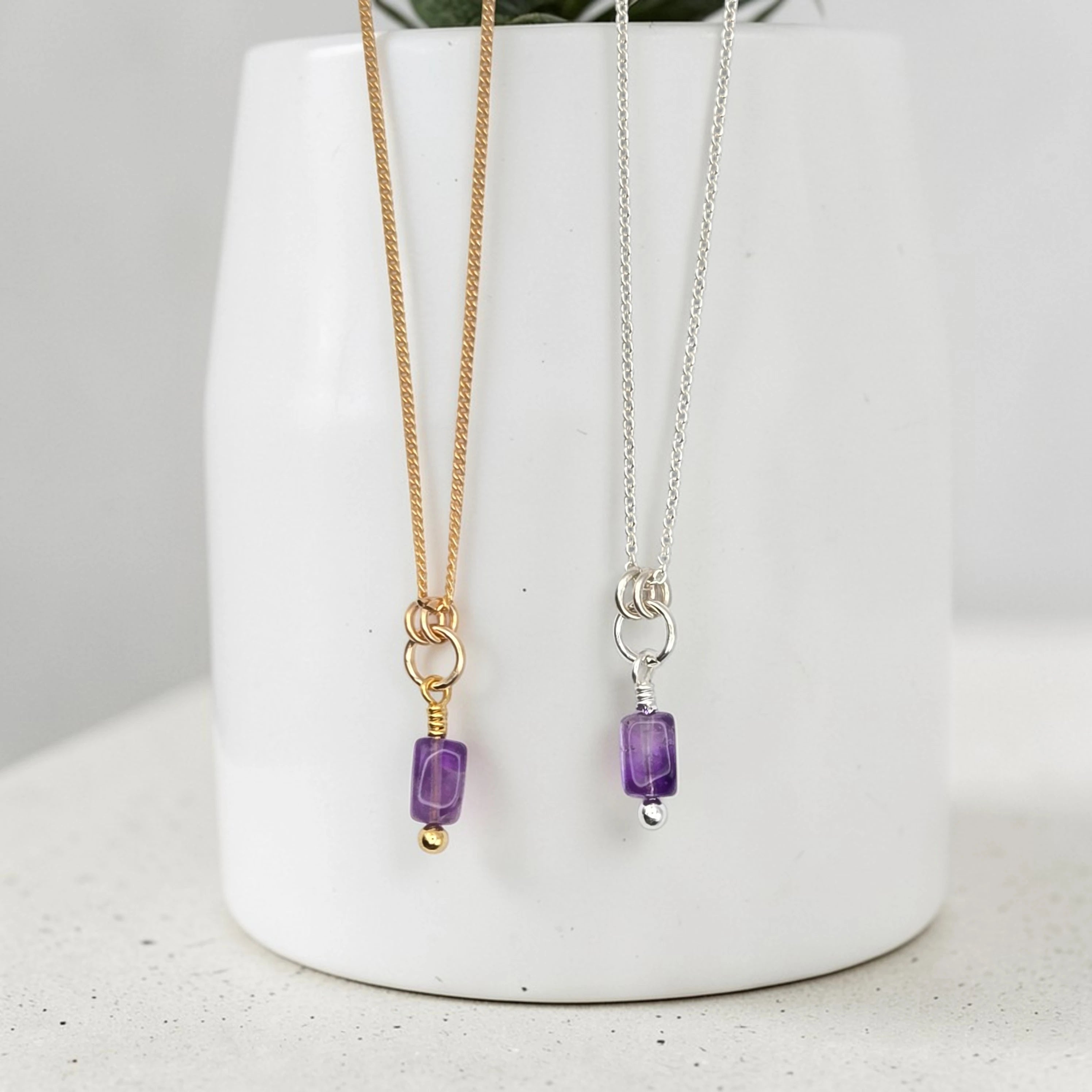 Two necklaces with purple beads on a white vase