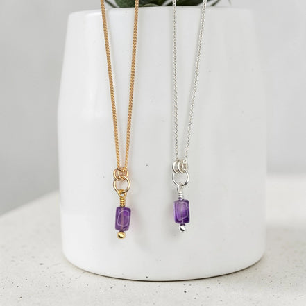 Two necklaces with purple beads on a white vase