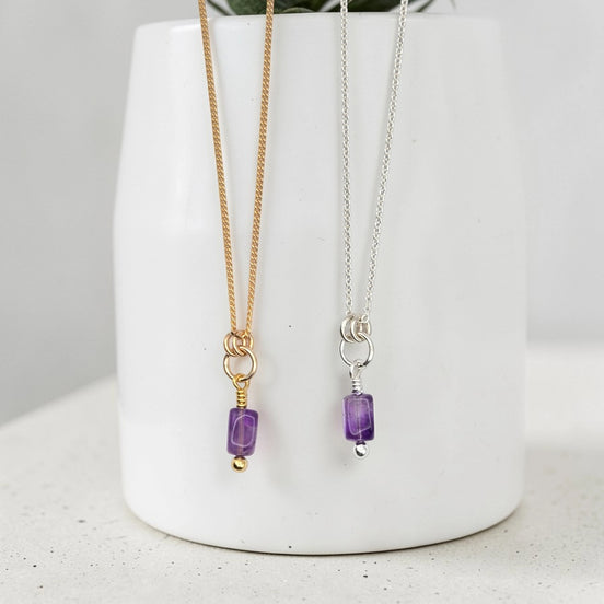 Two necklaces with purple beads on a white vase