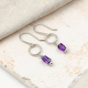 Silver earrings with purple amethyst beads on a marble surface