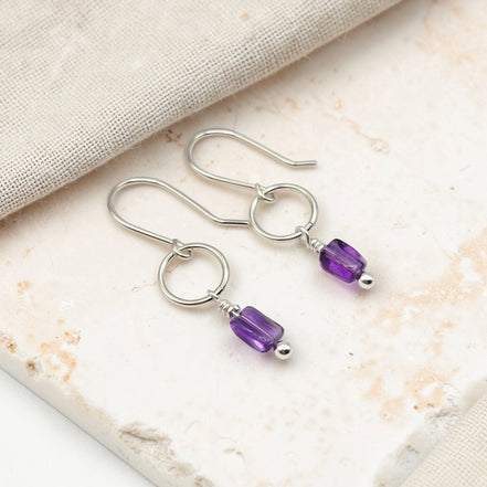 Silver earrings with purple amethyst beads on a marble surface