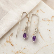Silver earrings with purple amethyst beads on a marble surface