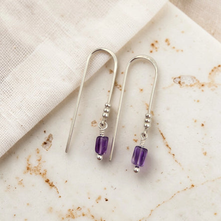 Silver earrings with purple amethyst beads on a marble surface