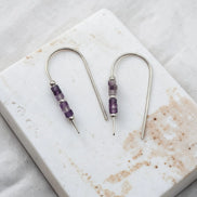Pair of silver earrings with purple beads on a marble surface