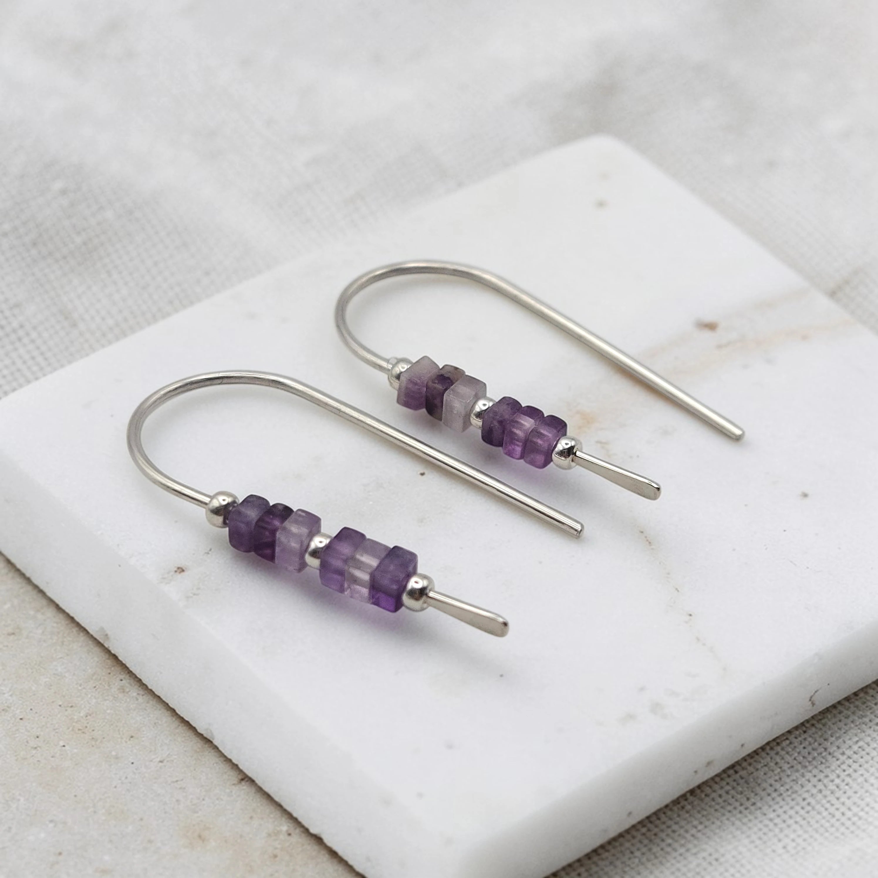 Pair of silver earrings with purple amethyst beads on a marble surface