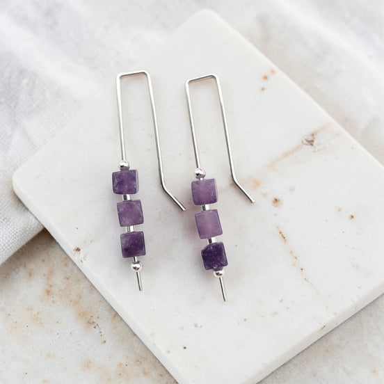 Pair of silver earrings with purple amethyst cube beads on a marble surface