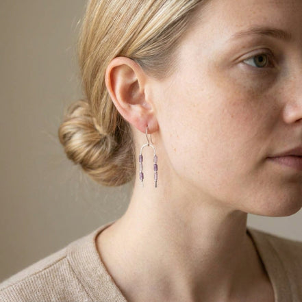 Bijou by SAM handcrafted sterling silver wishbone earrings featuring delicate purple amethyst tube stones on a model