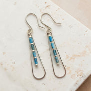 Bijou by SAM Still Water teardrop earrings with blue Apatite tube beads and sterling silver hoops on stone surface.