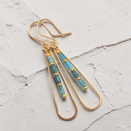 Bijou by SAM Still Water teardrop earrings with blue Apatite tube beads and 14k gold fill hoops on textured surface