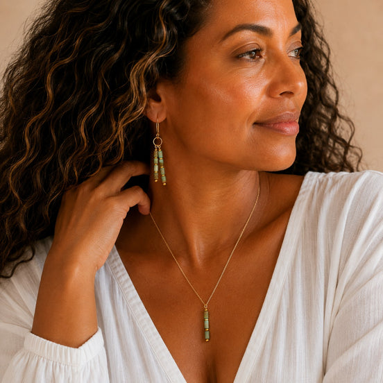 Bijou by SAM Big Sky earrings featuring aqua terra jasper tube beads on gold hoops worn by a woman in a white top