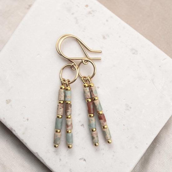 Bijou by SAM Big Sky earrings featuring Aqua Terra Jasper tube beads and 14k gold fill hoops on a white stone base.