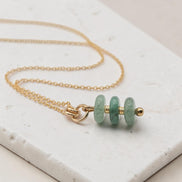Bijou by SAM Comet necklace featuring three green aventurine stones on a delicate gold fill chain on a stone surface.