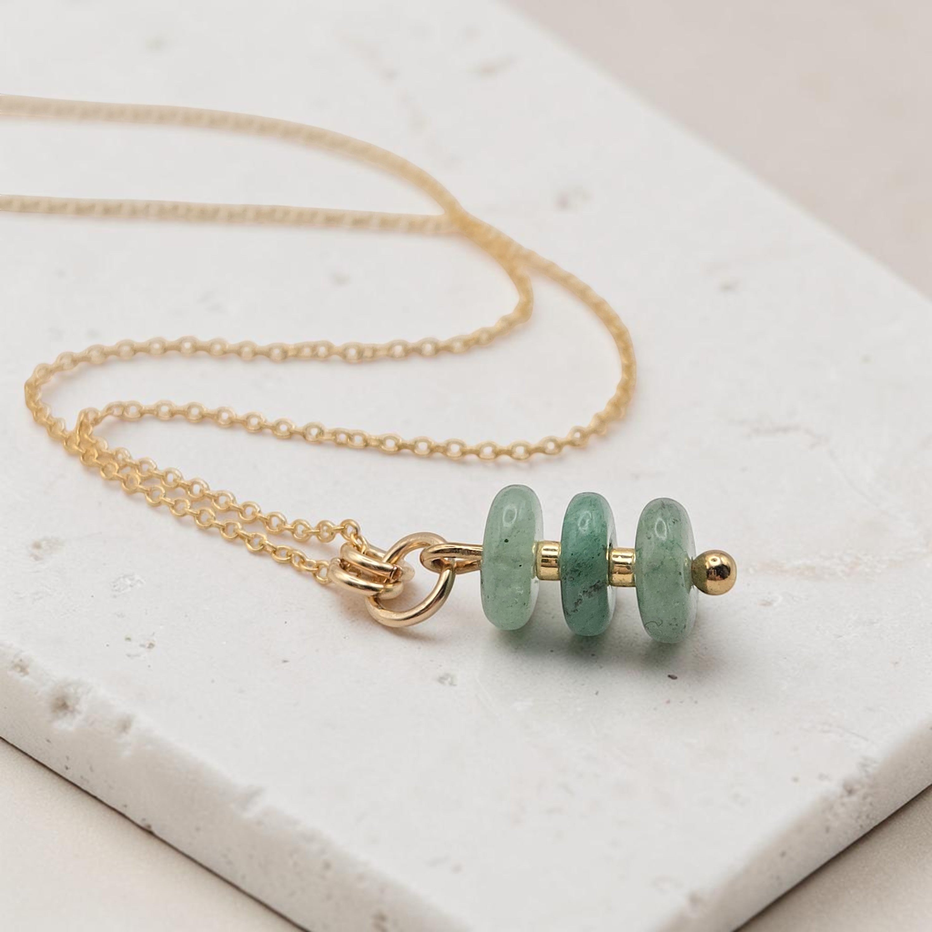 Bijou by SAM Comet necklace featuring three green aventurine stones on a delicate gold fill chain on a stone surface.