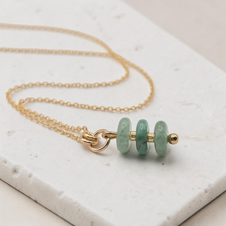 Bijou by SAM Comet necklace featuring three green aventurine stones on a delicate gold fill chain on a stone surface.