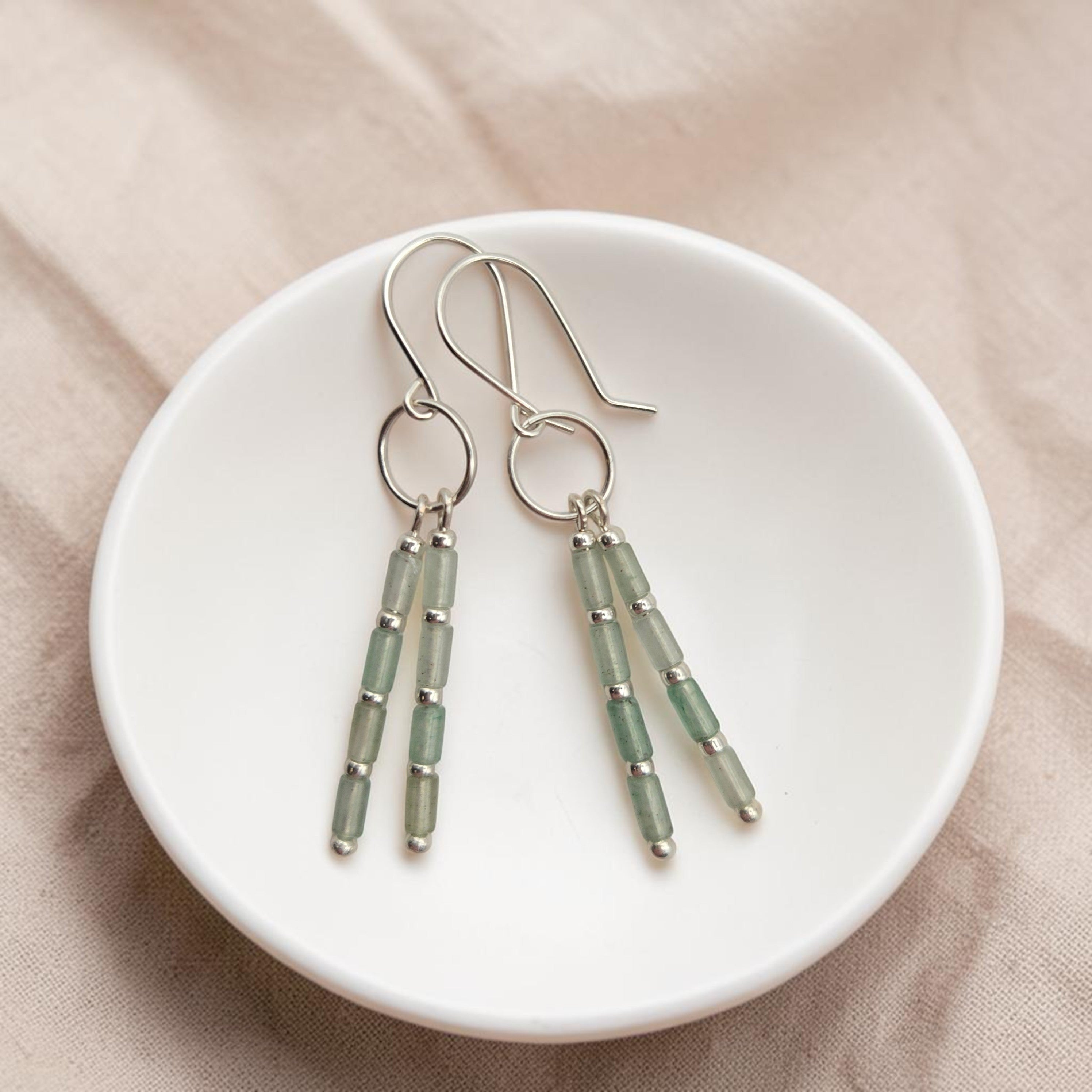 Bijou by SAM Mossy Creek earrings featuring green aventurine tube beads and sterling silver hoops in a white bowl.