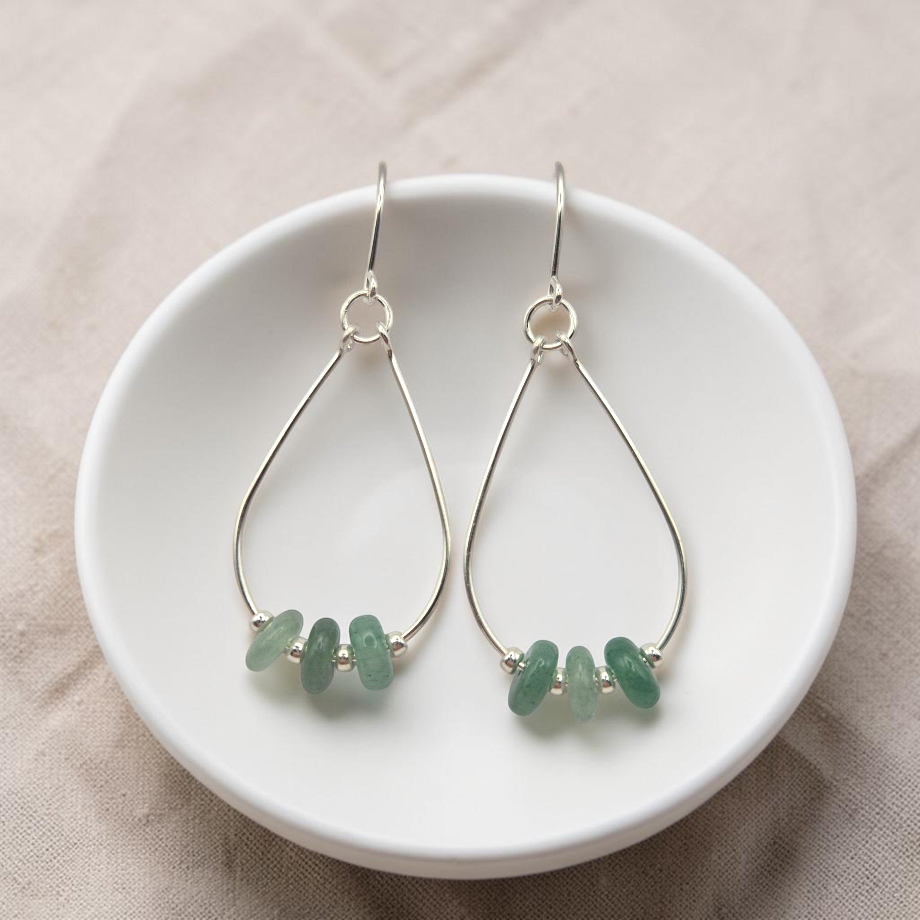 Bijou by SAM Comet Teardrop Hoop Earrings featuring green aventurine stones on sterling silver wire in a white dish.