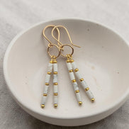 Bijou by SAM First Snow earrings featuring white howlite tube beads and 14k gold fill hoops in a ceramic bowl.