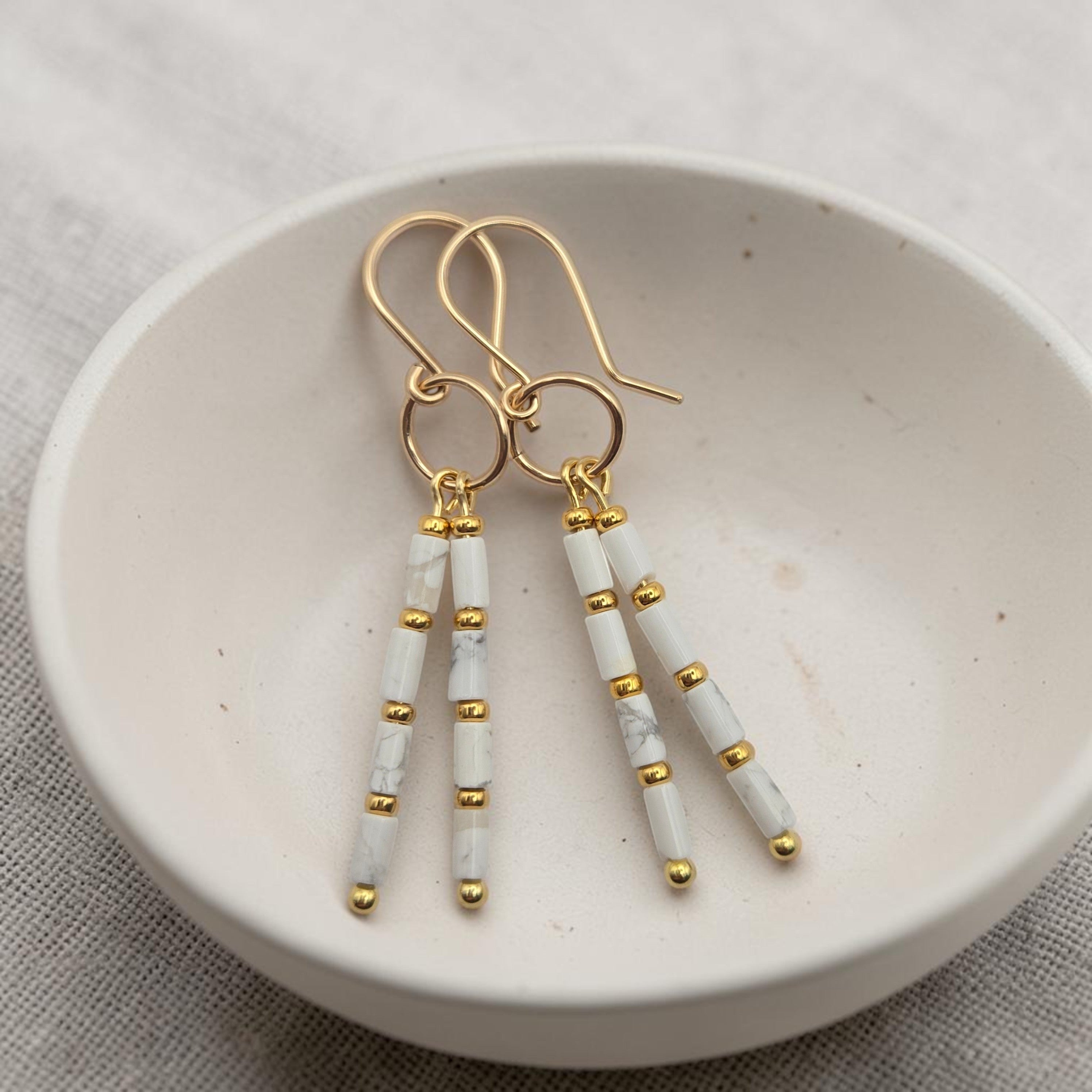 Bijou by SAM First Snow earrings featuring white howlite tube beads and 14k gold fill hoops in a ceramic bowl.