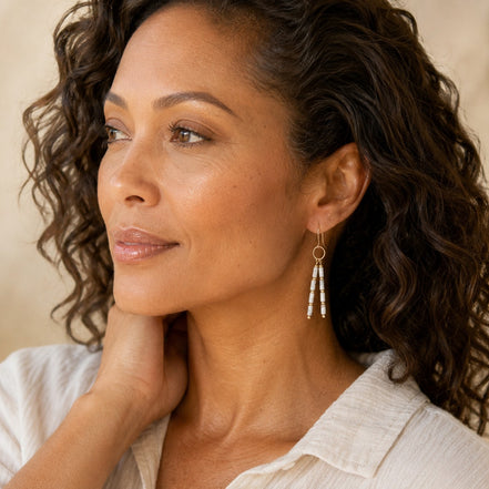 Bijou by SAM First Snow earrings featuring white Howlite tube beads and gold hoops worn by a woman with curly hair.