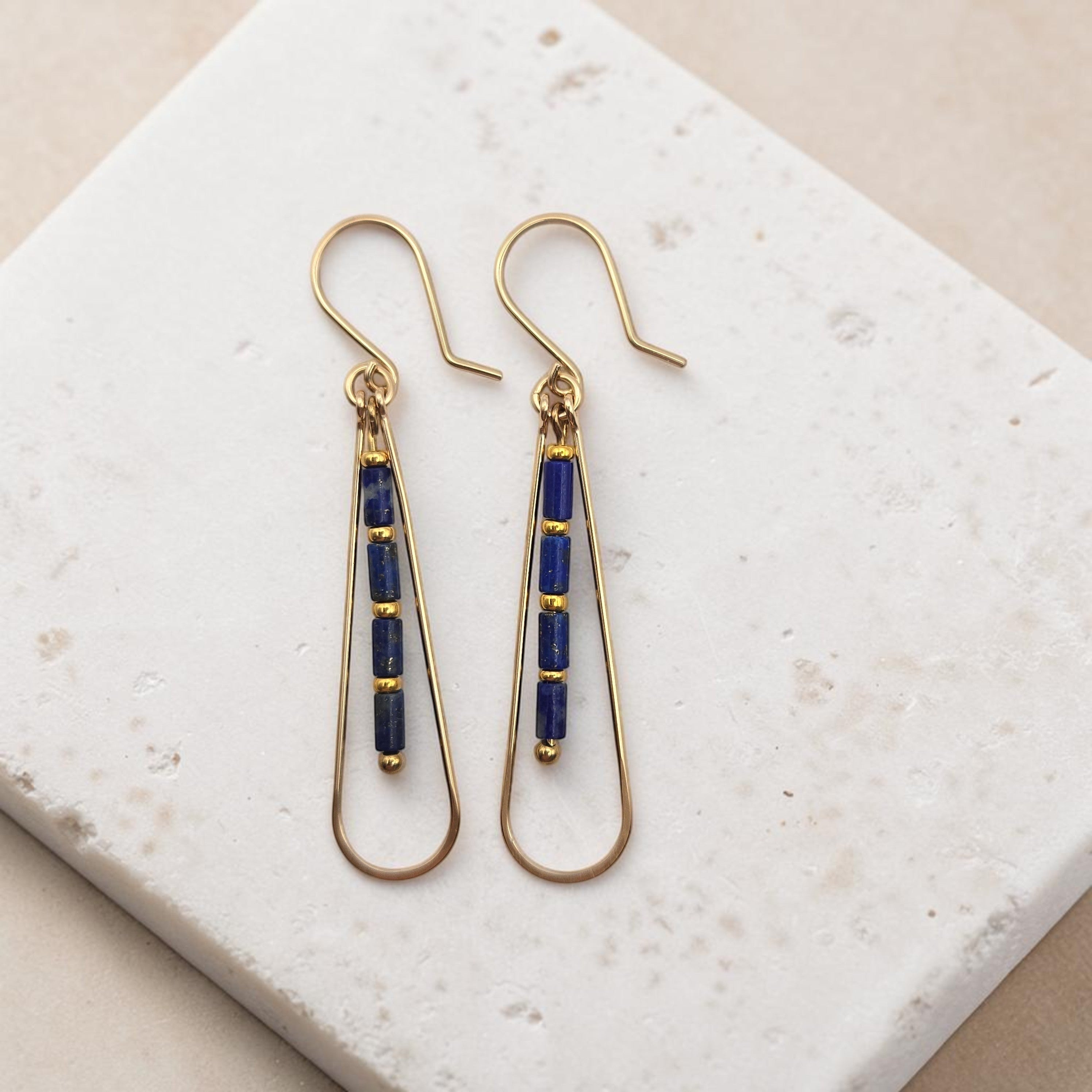 Bijou by SAM Midnight Sky teardrop earrings with blue Lapis Lazuli beads and 14k gold fill hoops on a stone surface.