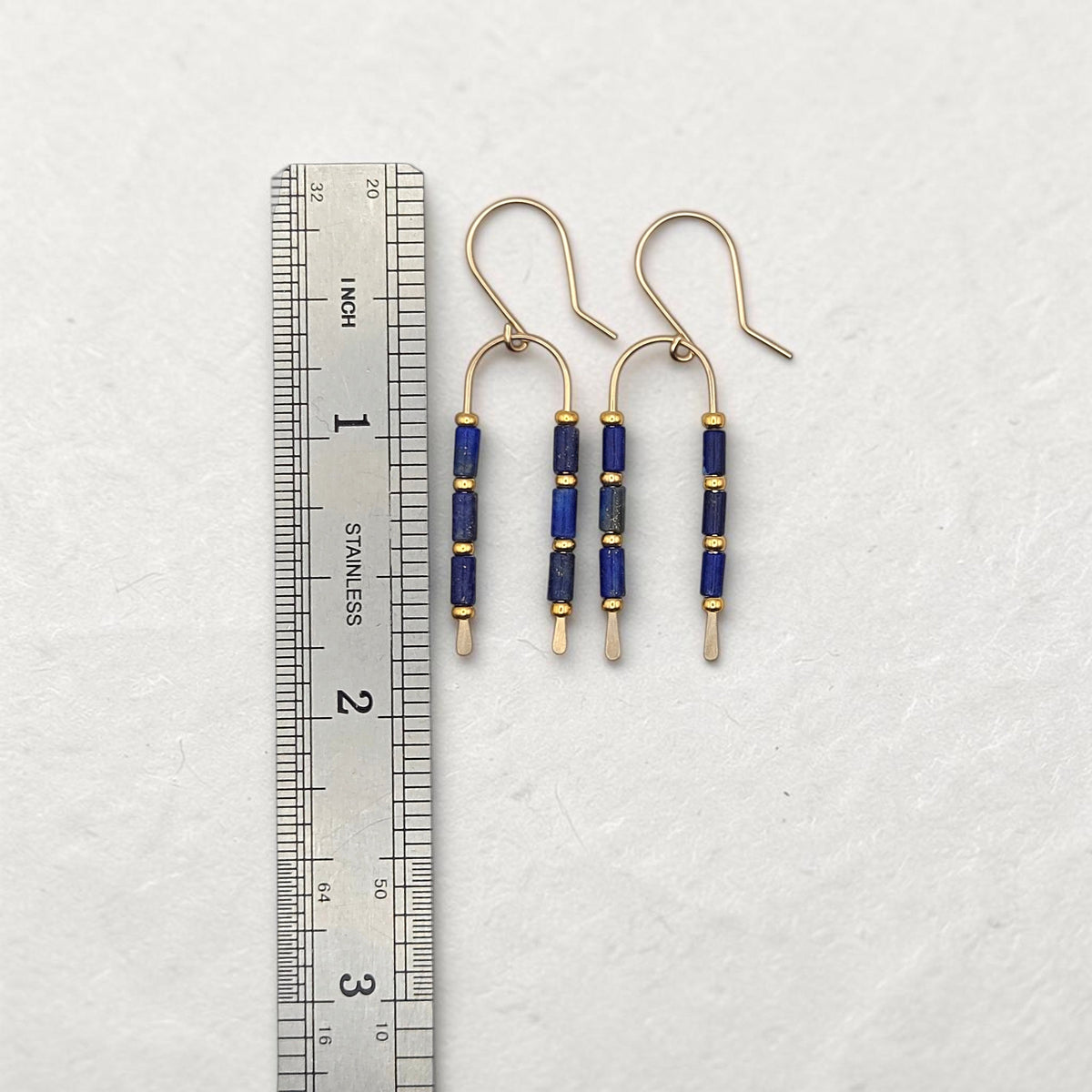 Bijou by SAM wishbone earrings featuring blue lapis lazuli tube stones and gold fill wire next to a metal ruler.