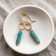 Bijou by SAM Mia earrings featuring turquoise jasper cylinders on handcrafted 14k gold fill hoops in a white bowl.