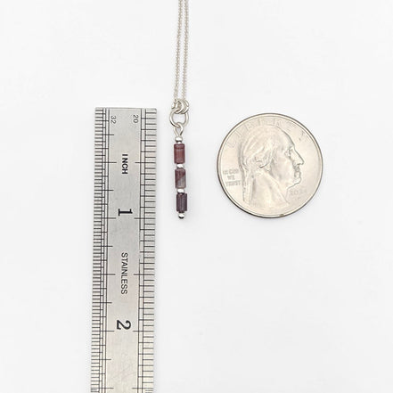 Bijou by SAM Painted Bluff necklace with natural red rainbow jasper tube beads and sterling silver chain next to a coin