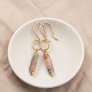 Bijou by SAM Olivia earrings featuring cylindrical Redline Jasper stones on 14k gold fill hoops in a white dish.