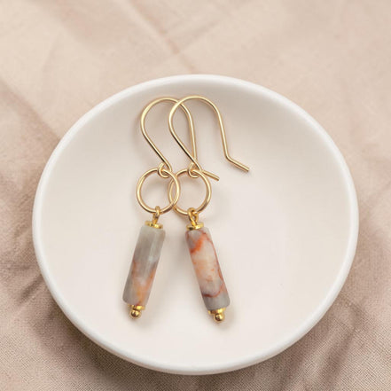 Bijou by SAM Olivia earrings featuring cylindrical Redline Jasper stones on 14k gold fill hoops in a white dish.