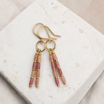 Bijou by SAM Rose Bluff earrings featuring pink rhodonite tube beads and 14k gold fill hoops on a stone display.