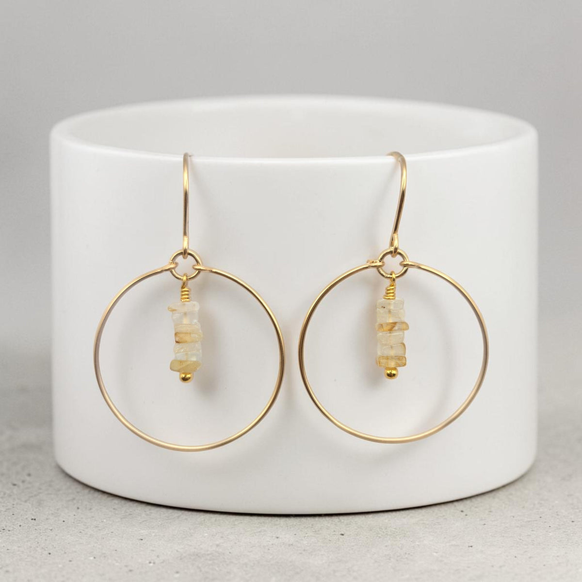 Bijou by SAM handmade gold hoop earrings featuring delicate square-cut rutilated quartz stones on a white stand.