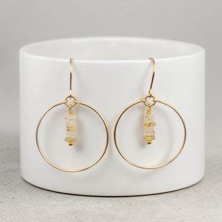 Bijou by SAM handmade gold hoop earrings featuring delicate square-cut rutilated quartz stones on a white stand.