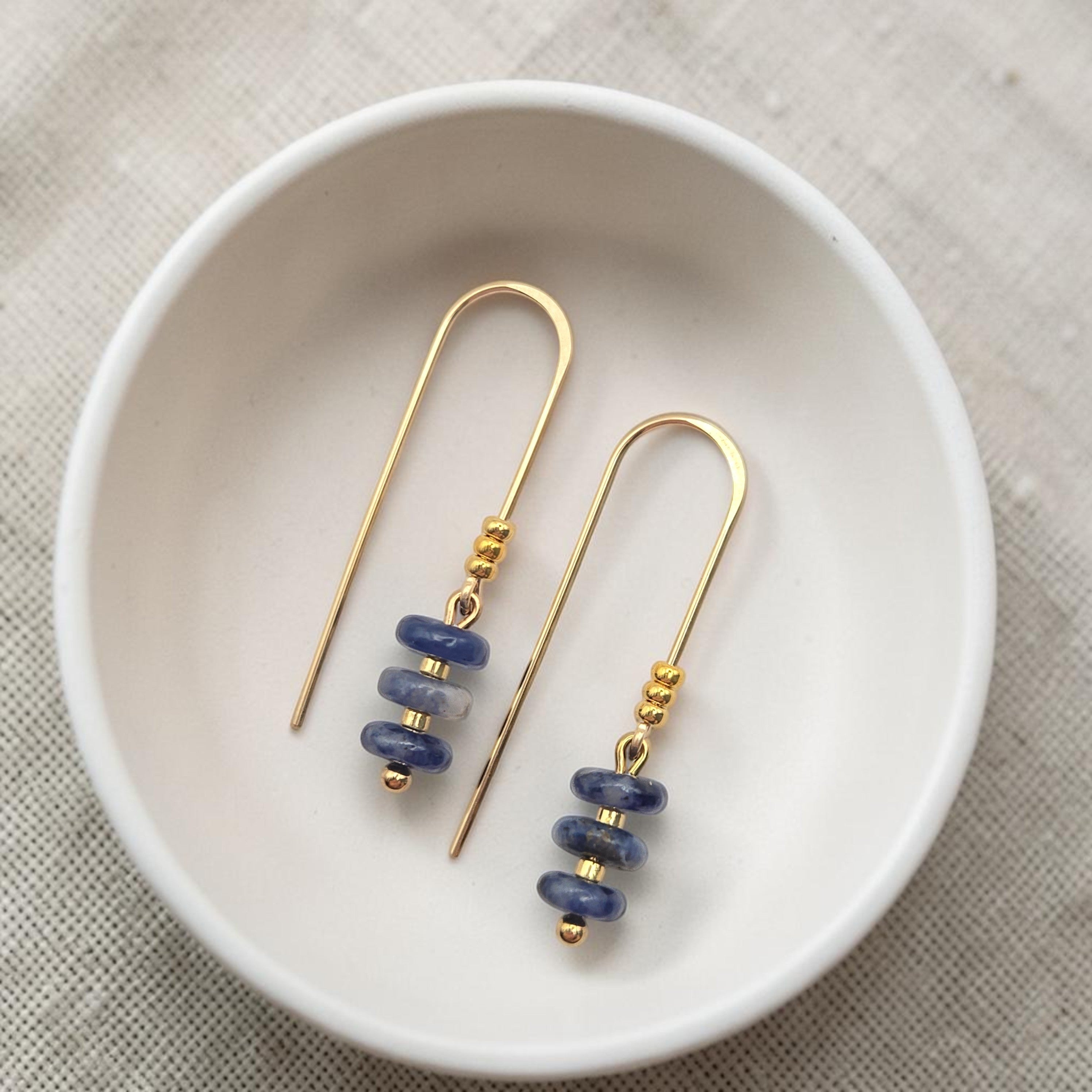 Bijou by SAM Milky Way threader earrings featuring deep blue sodalite beads on 14k gold filled wire in a white dish.
