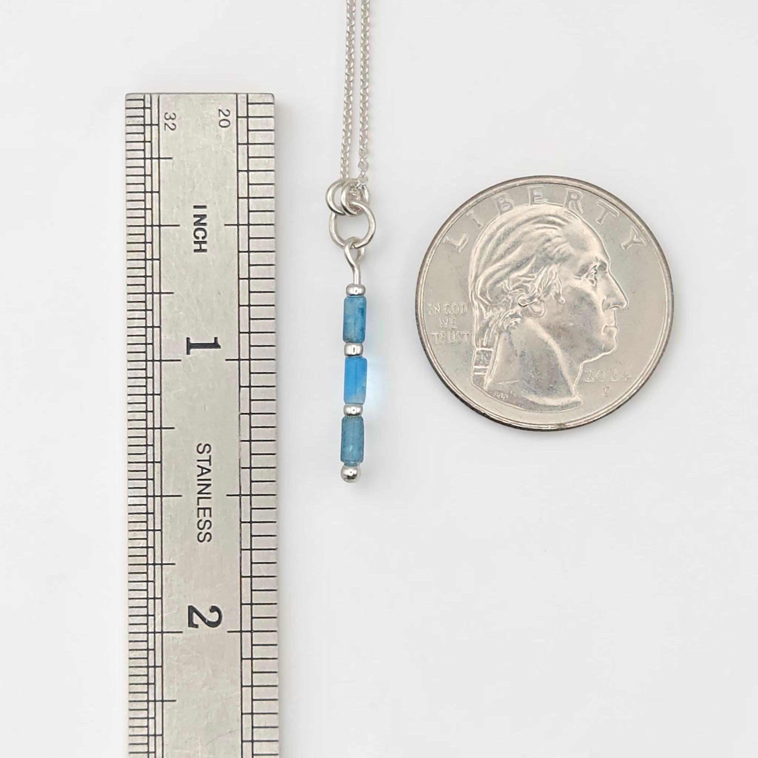 Bijou by SAM Still Water necklace with blue apatite tube beads on a sterling silver chain next to a ruler and coin.