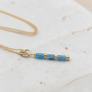 Bijou by SAM Still Water necklace featuring blue apatite tube beads and 14k gold fill chain on a textured surface.