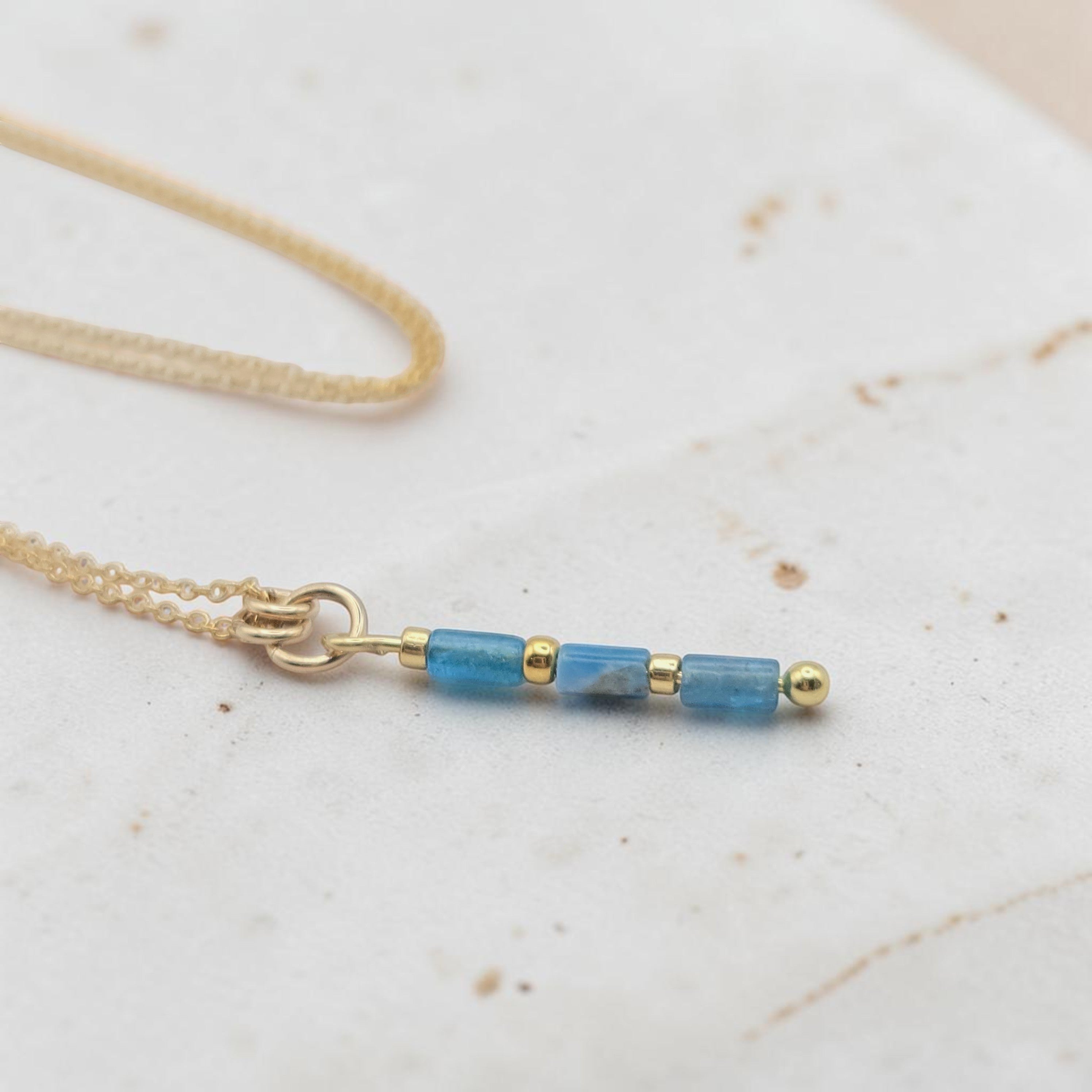 Bijou by SAM Still Water necklace featuring blue apatite tube beads and 14k gold fill chain on a textured surface.