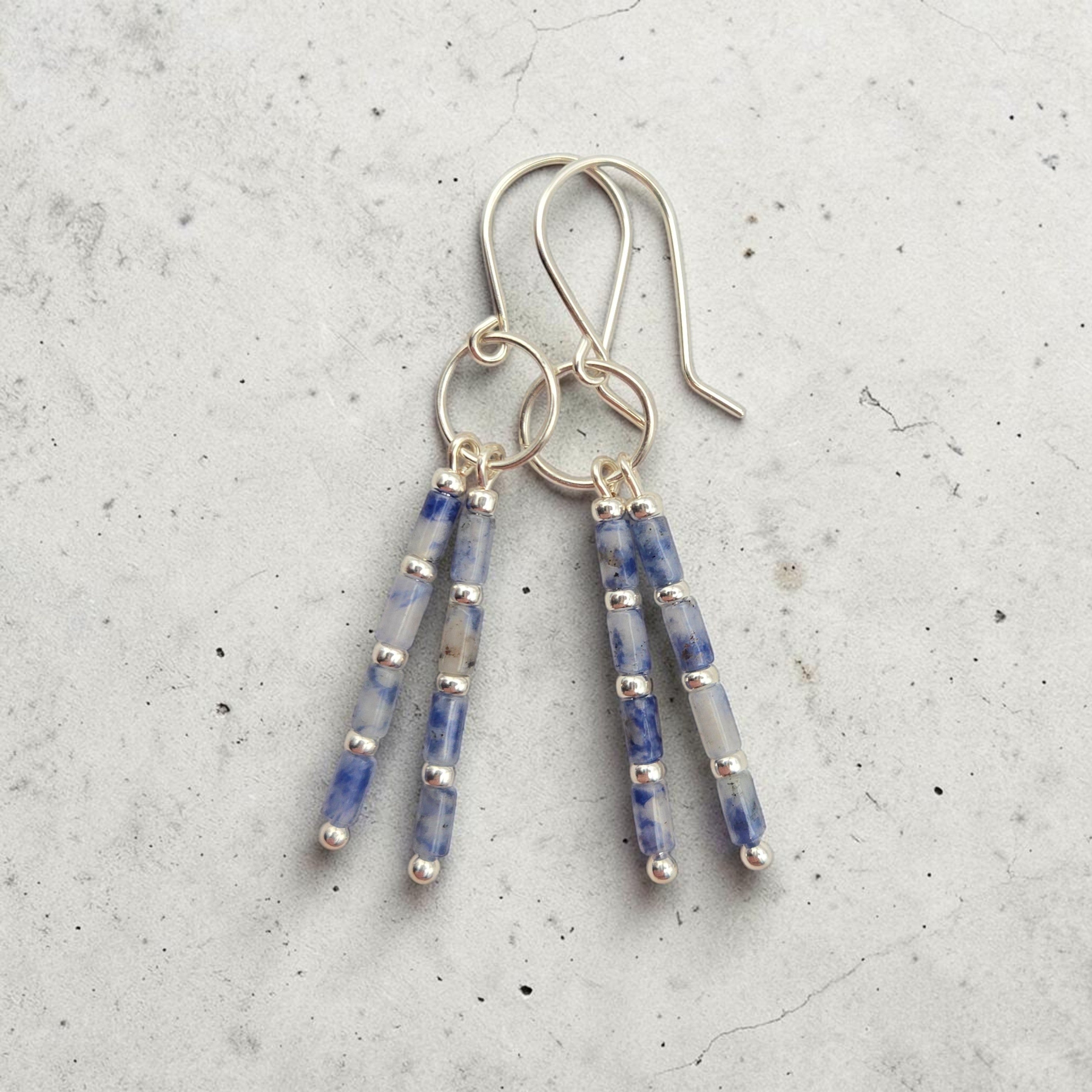 Bijou by SAM Stone Creek earrings with blue spot jasper tube beads and sterling silver hoops on a grey background.